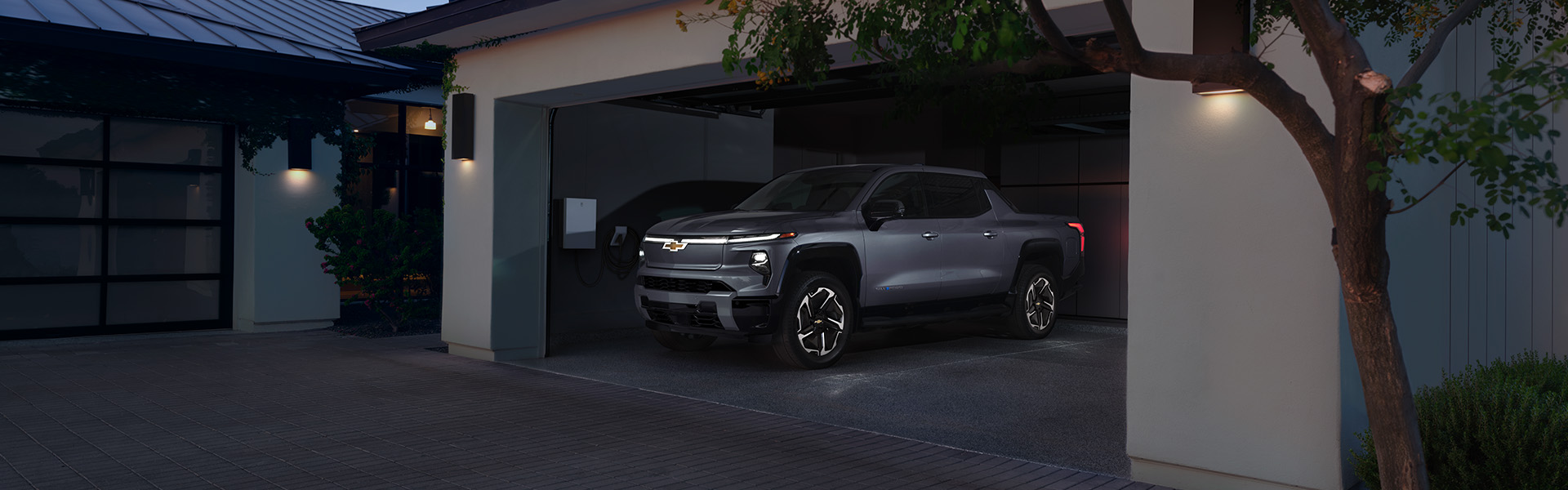 A silver 2025 Chevrolet Silverado electric pickup truck parked in a modern garage at dusk.