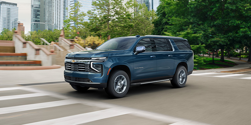 A 2026 Chevrolet Suburban driving down a bustling city street, showcasing its sleek design and urban environment.