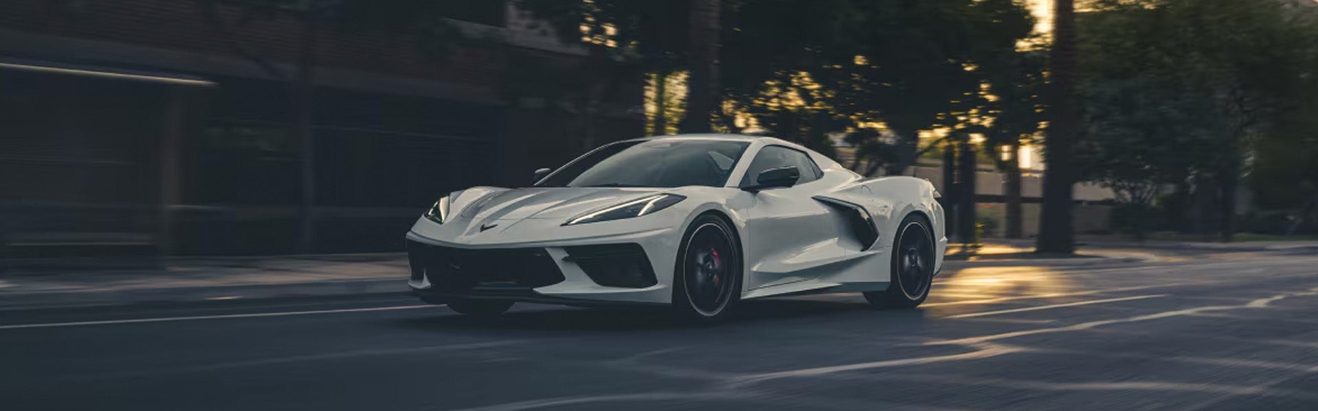White Chevrolet Corvette Stingray convertible driving on a road at sunset.