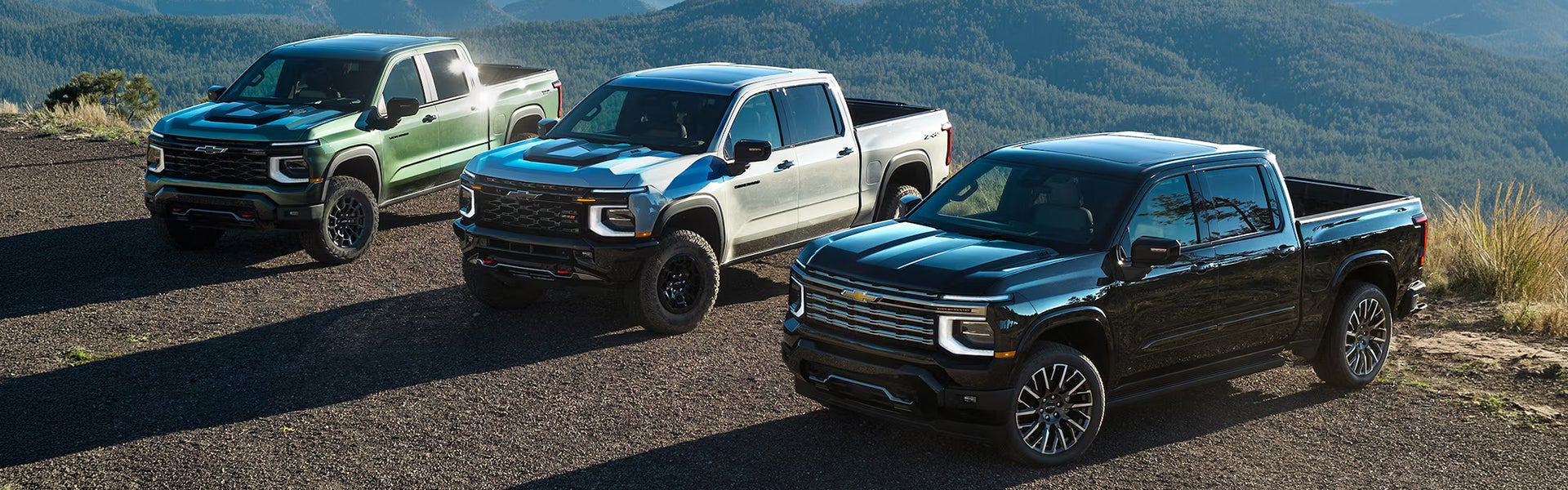 Three 2027 Chevrolet Silverado 1500 parked on scenic mountain landscape.